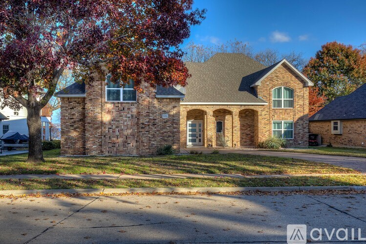 A house with a stone wall and a tree with red leaves in front.