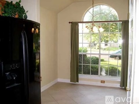 A black refrigerator is in a kitchen next to a window with a view of a yard.
