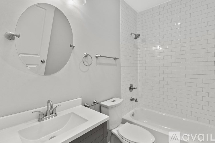 A white bathroom with a round mirror, sink, toilet, and bathtub.