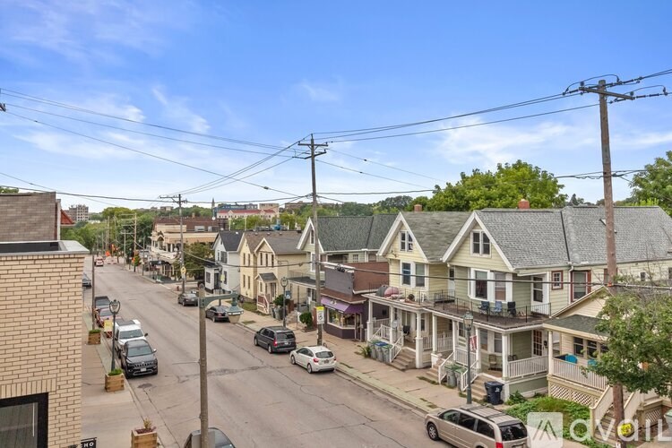 A street view of a residential area with houses on both sides and cars parked along the curb.