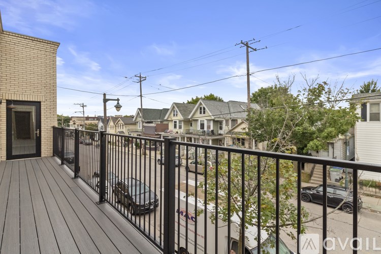 A balcony with a black railing overlooks a street with cars and houses.