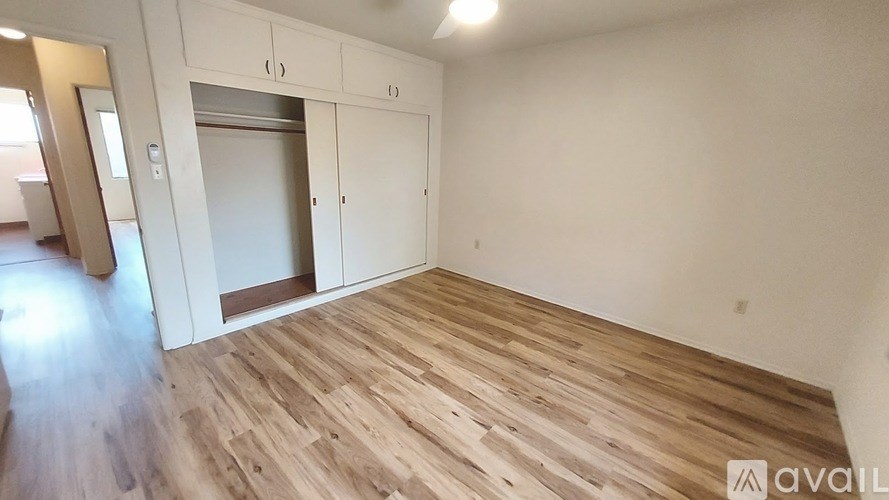A room with wooden flooring and white walls, with a door leading to another room.
