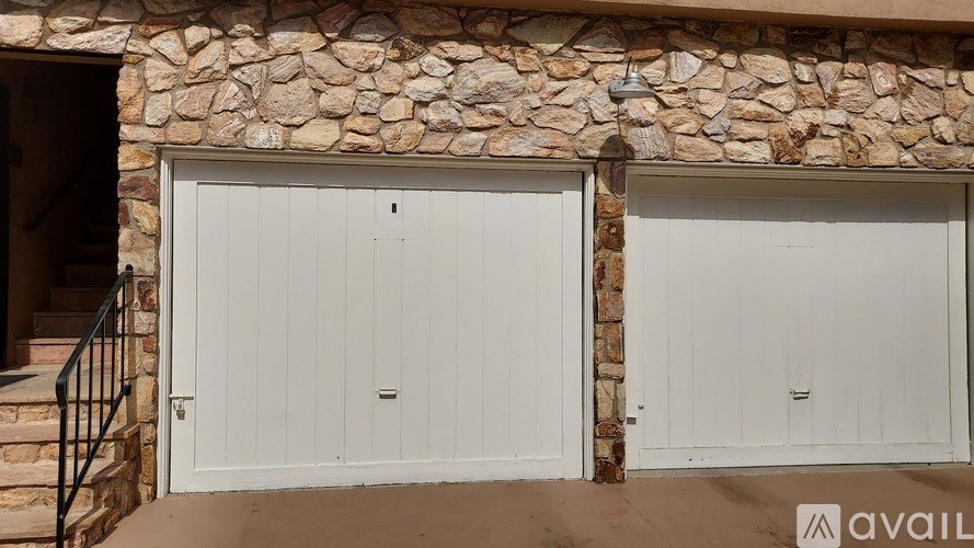 Two white garage doors are closed and situated between two stone walls.