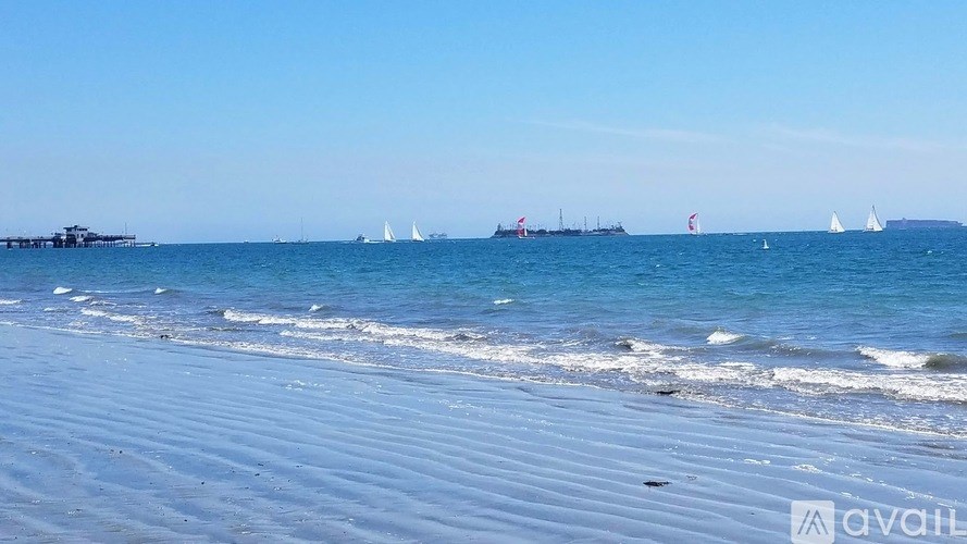 A beach scene with boats in the water and a pier in the distance.