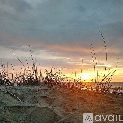 The image shows a beach at sunset with the sun setting over the horizon.