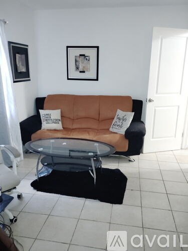 A living room with a brown couch and a black and white picture on the wall.