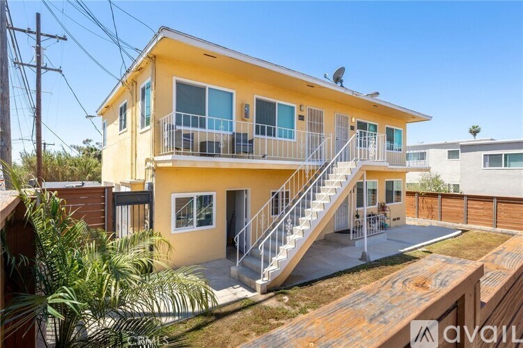 A yellow house with a balcony and stairs leading to the front door.