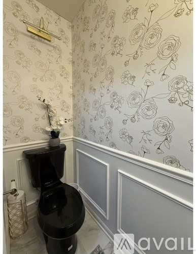 A black toilet in a bathroom with floral wallpaper.