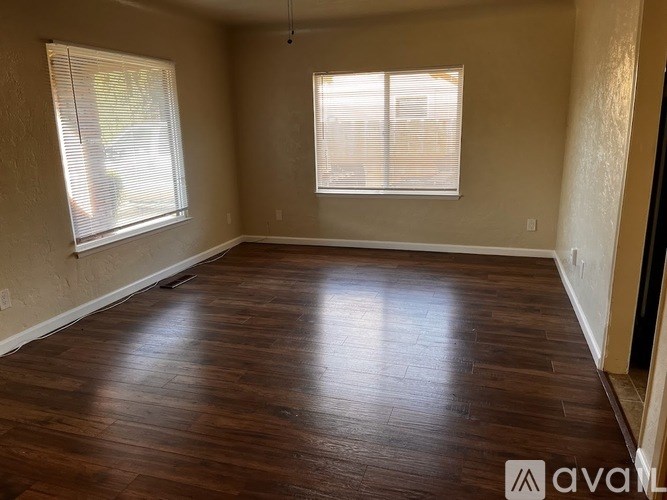 A room with wooden flooring and two windows.