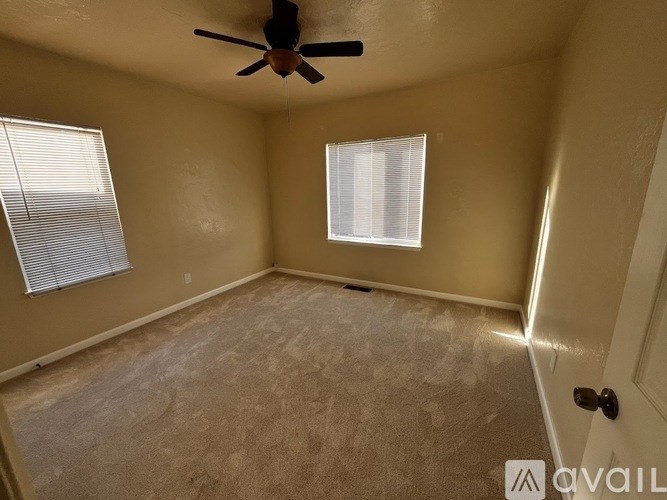 A room with a ceiling fan and two windows.