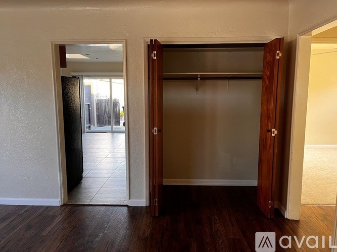 A room with a wooden floor and a white wall with a door open to a balcony.