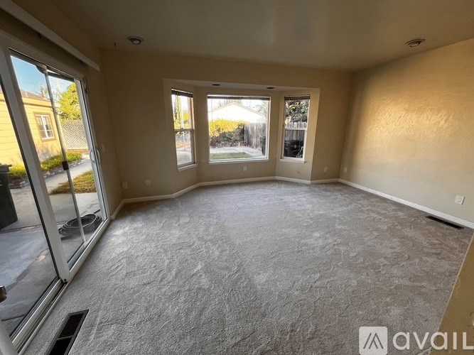 A spacious room with a grey carpet and large windows.