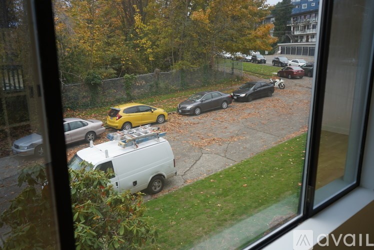 A view from a window looking out at a parking lot with cars and a white van.