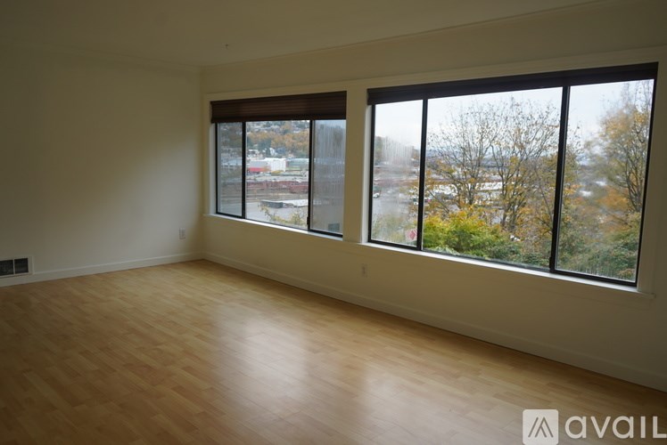 A room with wooden floors and two windows overlooking a parking lot and trees.