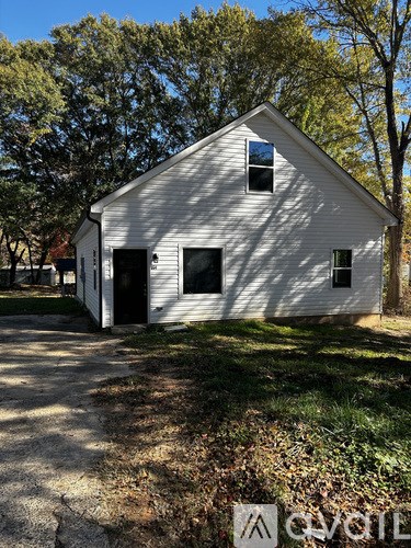 A white barn-like building with a black door and windows is surrounded by trees.