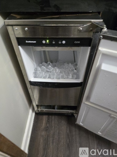 A stainless steel ice maker with a digital display and a glass filled with ice.