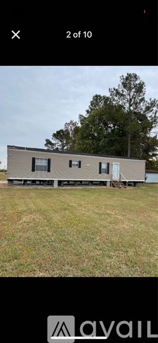 A house with a grey roof and white walls is surrounded by grass.