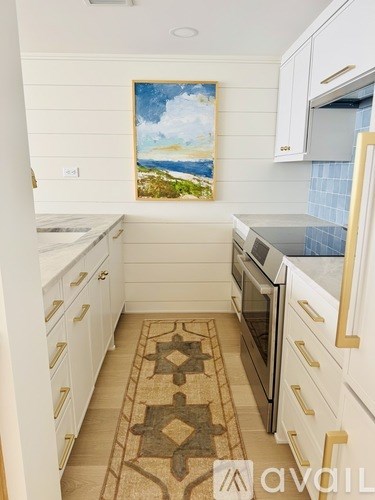 A kitchen with white cabinets and a painting of a beach scene on the wall.