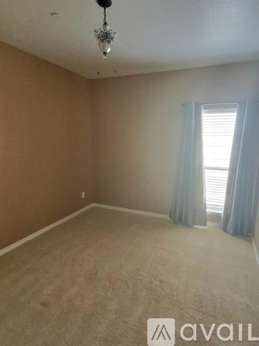 A room with a chandelier, carpeted floor, and a window with curtains.