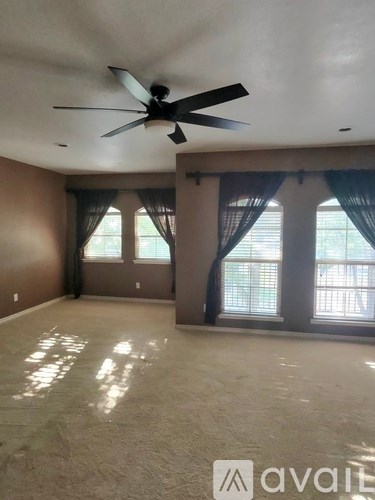 A room with a ceiling fan and large windows.