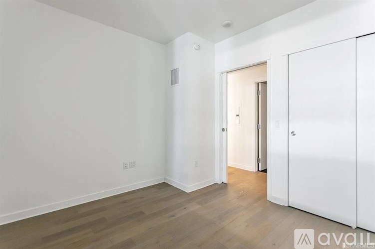 A room with white walls and wooden flooring, with a doorway leading to another room.