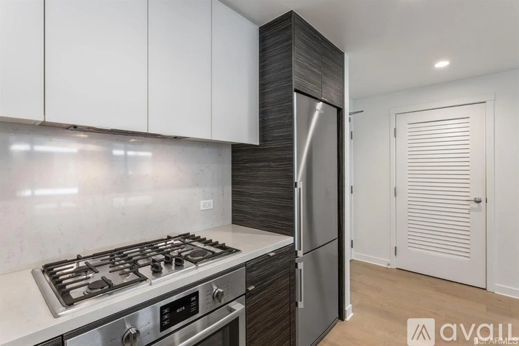 A modern kitchen with a stainless steel gas stove and a refrigerator with a dark wood finish.