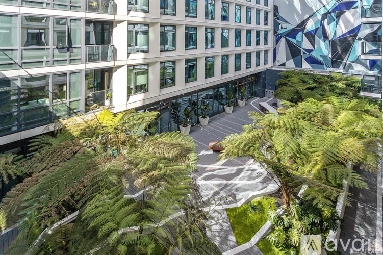 A modern building with a glass facade and a courtyard with ferns and a geometric sculpture.
