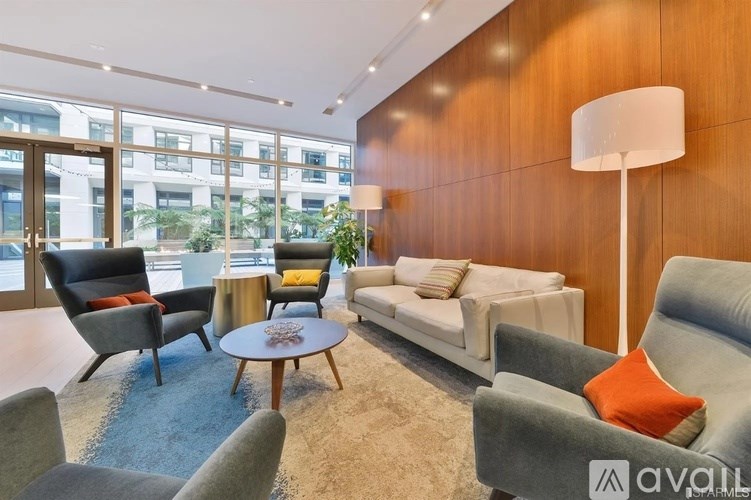 A living room with a grey sofa, a grey armchair, a black chair, a white couch, a round table, and a lamp.