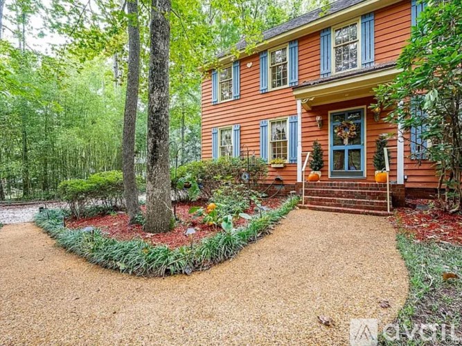 A red house with a blue door and windows is surrounded by trees and plants.