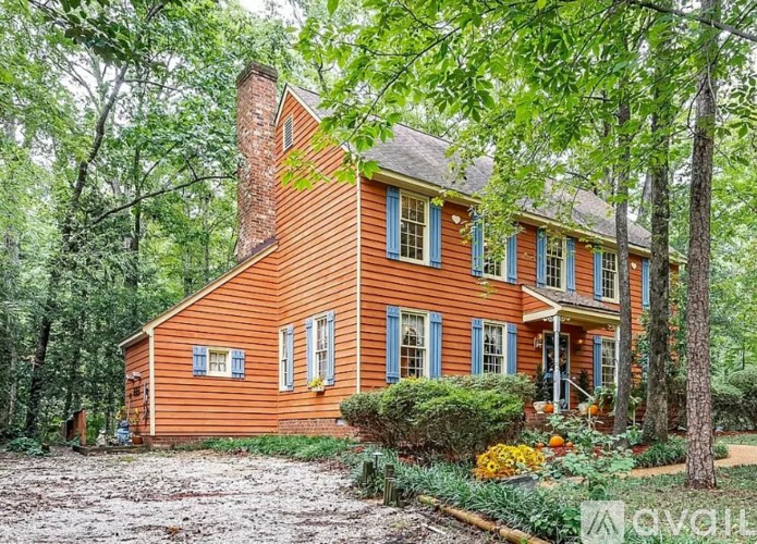 A red house with a chimney and a porch surrounded by trees.