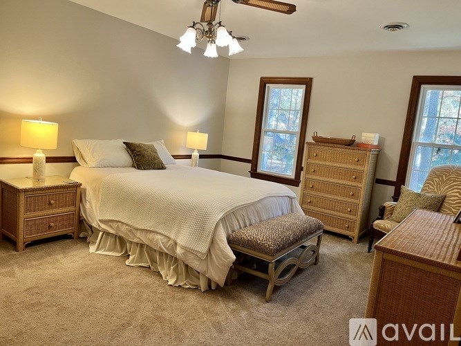 A bedroom with a large bed, a bench, and two windows.