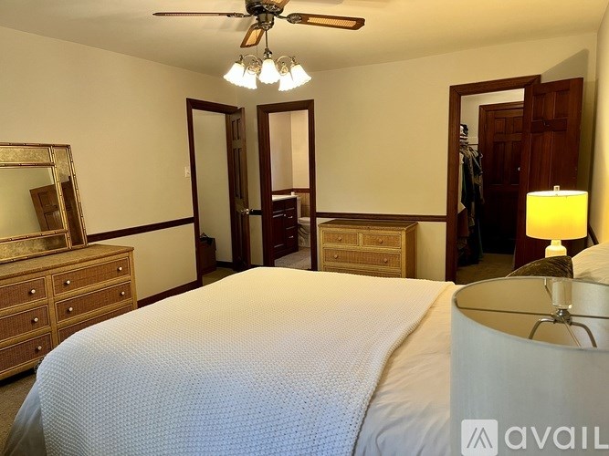 A bedroom with a large bed, a dresser, a mirror, and a ceiling fan.