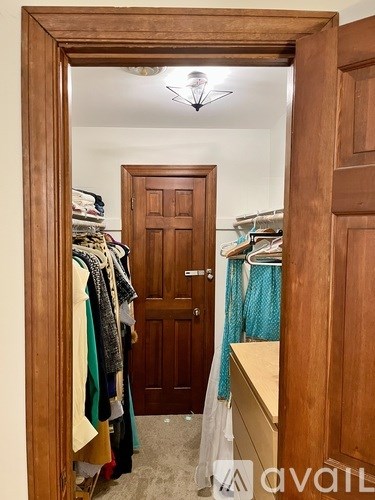 A wooden door is in a room with clothes hanging on a rack.
