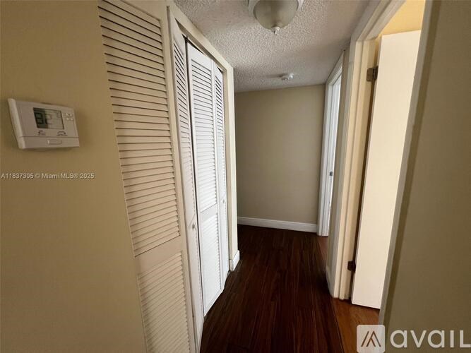 A hallway with a thermostat on the wall and wooden flooring.