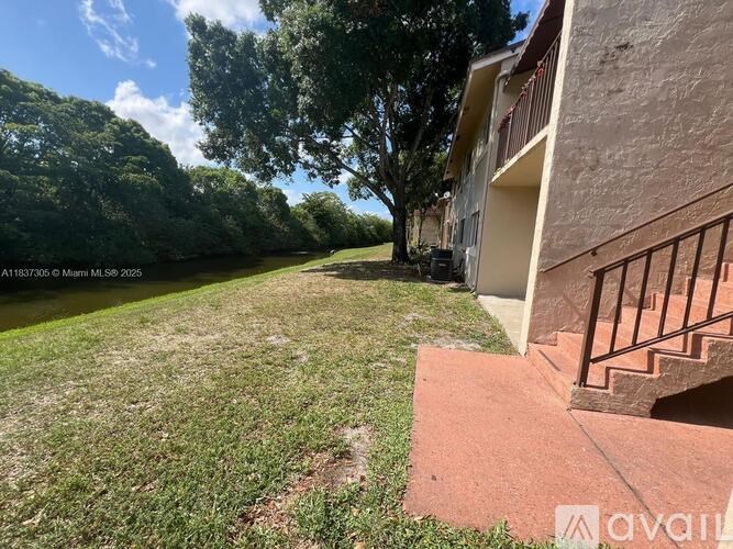 A building with a balcony overlooks a grassy area next to a body of water.