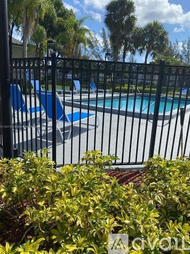 A pool surrounded by a black fence and green bushes.