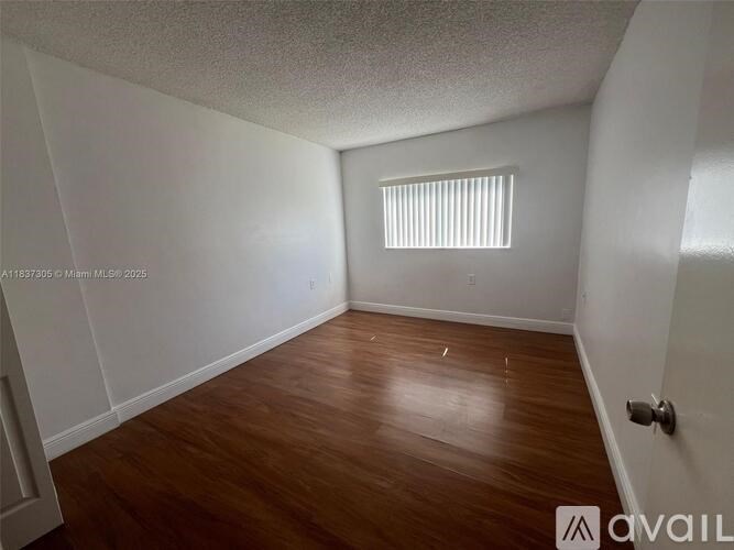 A room with wooden flooring and a window with blinds.