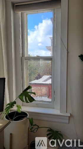 A window with a view of a red building and a cloudy sky.
