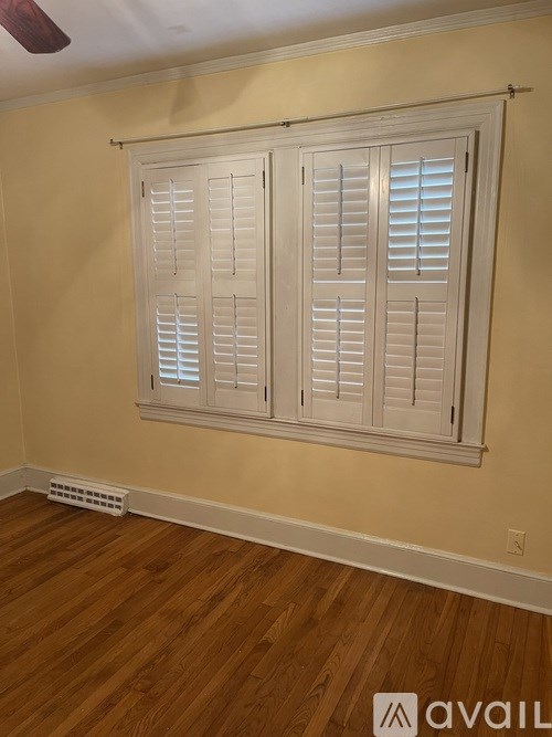 A room with a window covered by white shutters.