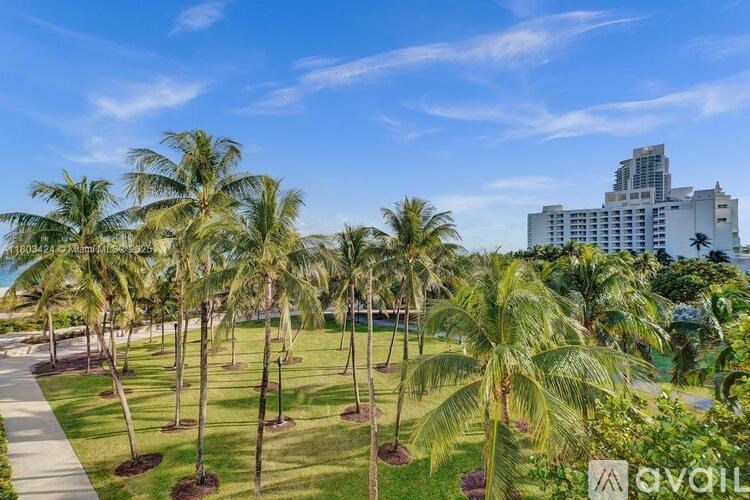 A row of palm trees in a park with a building in the background.