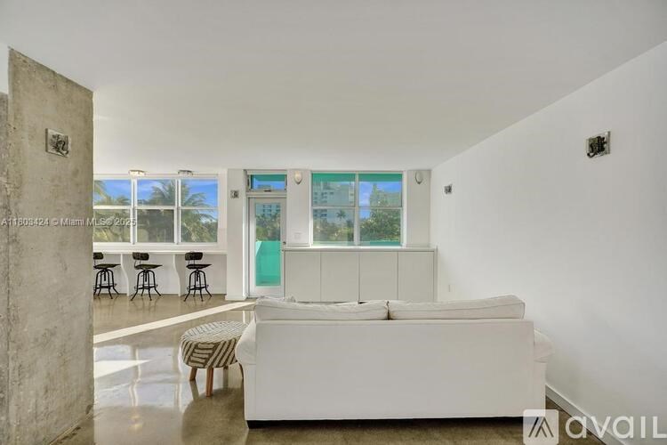 A white couch is in the middle of a room with a large window.