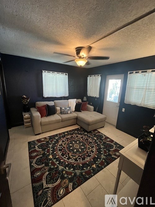 A living room with a rug on the floor and a fan on the ceiling.