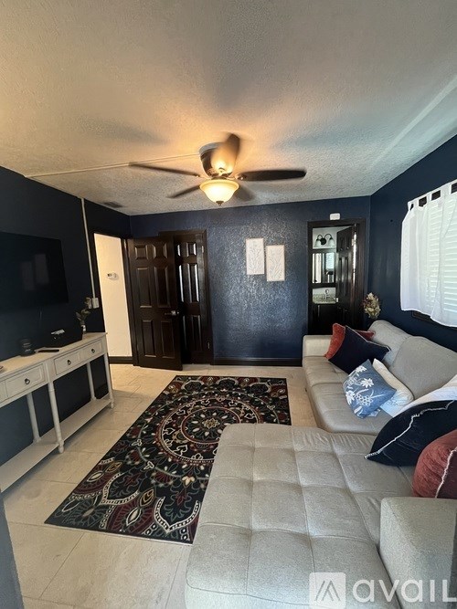 A living room with a rug, a couch, and a ceiling fan.