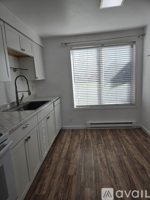 A kitchen with white cabinets and a window with blinds.