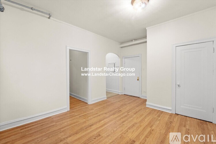 A room with wooden flooring and white walls, with a door on the left and a window on the right.