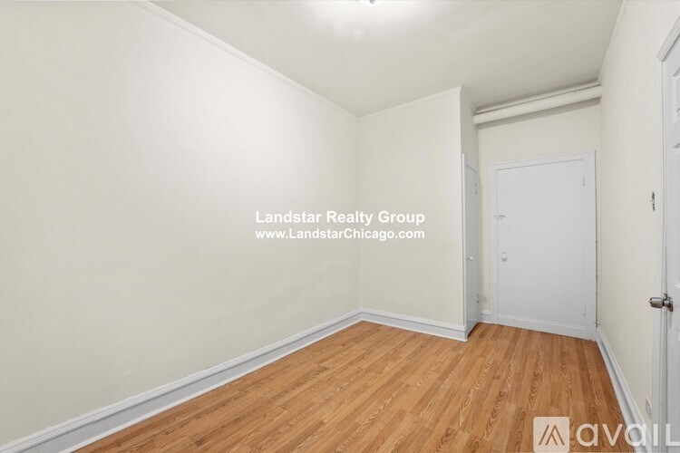 A room with wooden flooring and white walls, with a door on the right side.