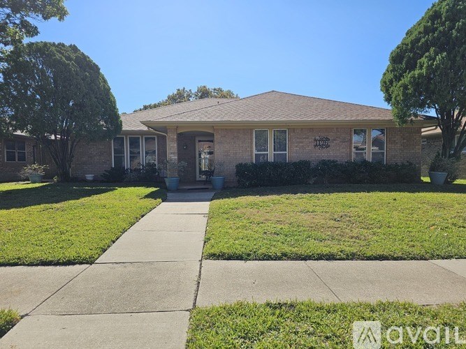 A house with a brown roof and a white door is surrounded by green grass and trees.