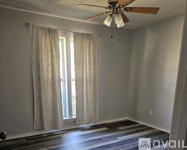 A room with a ceiling fan and a window with curtains.