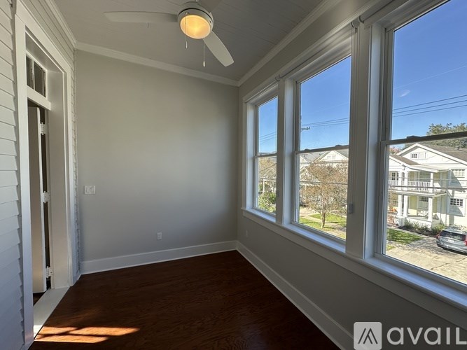 A room with a ceiling fan and large windows overlooking a residential street.
