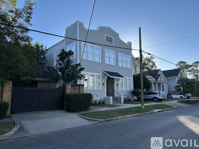 A house with a grey roof and white walls is surrounded by a black gate and a tree.